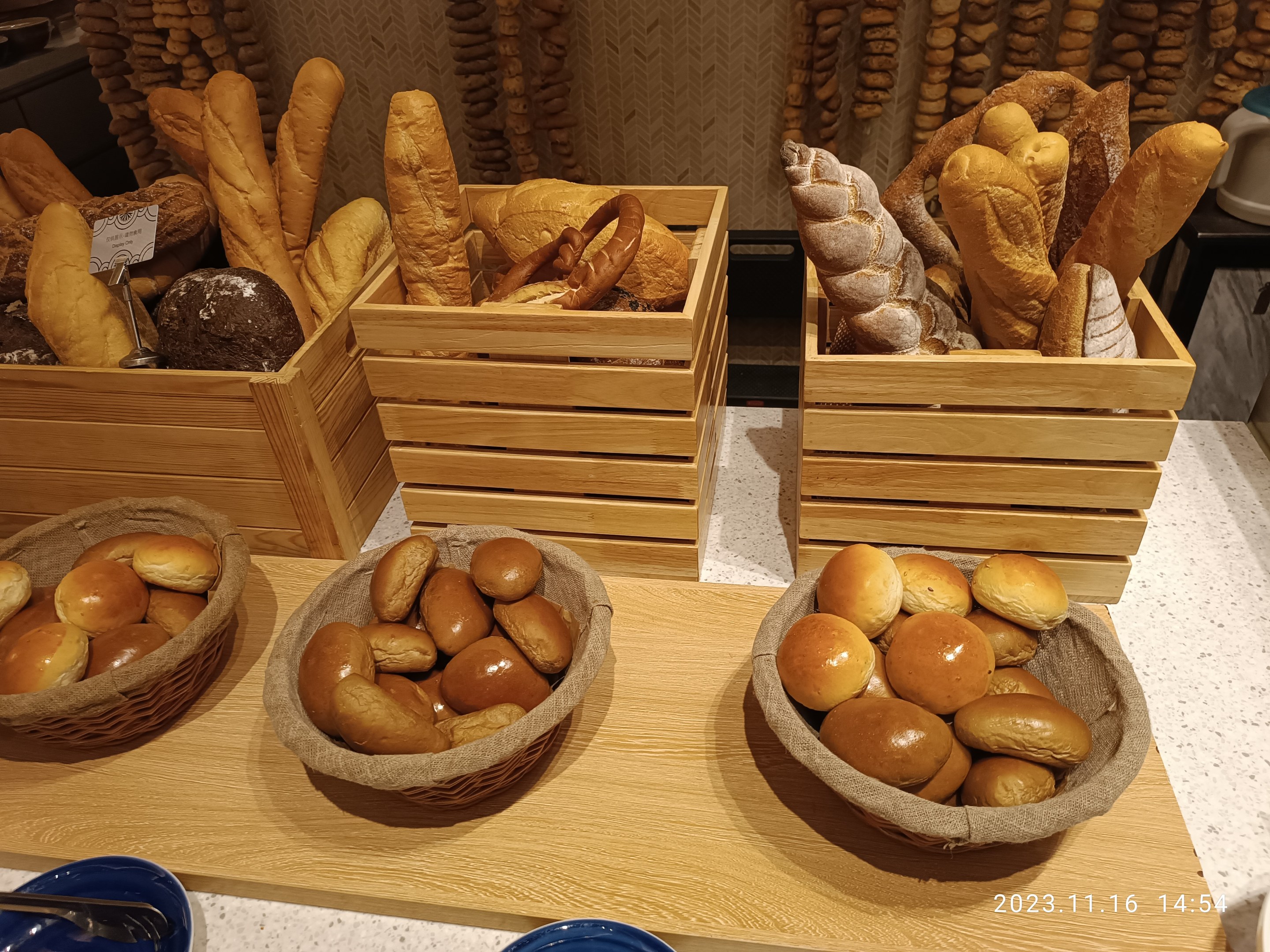 Holztisch mit Körben voller Brot, Tellern und Löffeln in einer Pariser Bäckerei mit einer gewässerten Wand im Hintergrund.