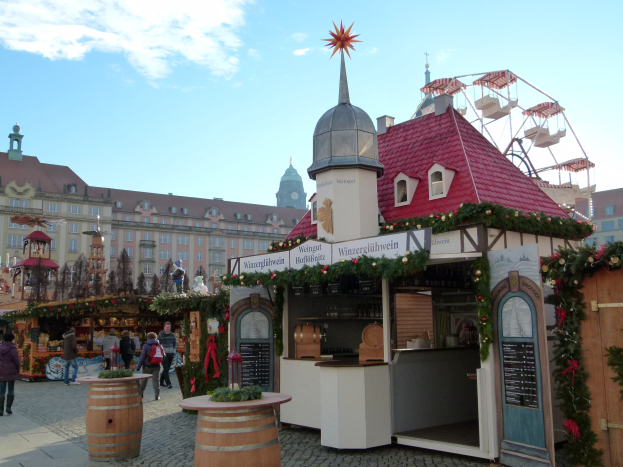 Ein geschäftiger Weihnachtsmarkt in Nürnberg, Deutschland mit Menschen um dekorierte Stände, festliche Lichter, ein Riesenrad, Gebäude und ein Schild am rechten Rand.