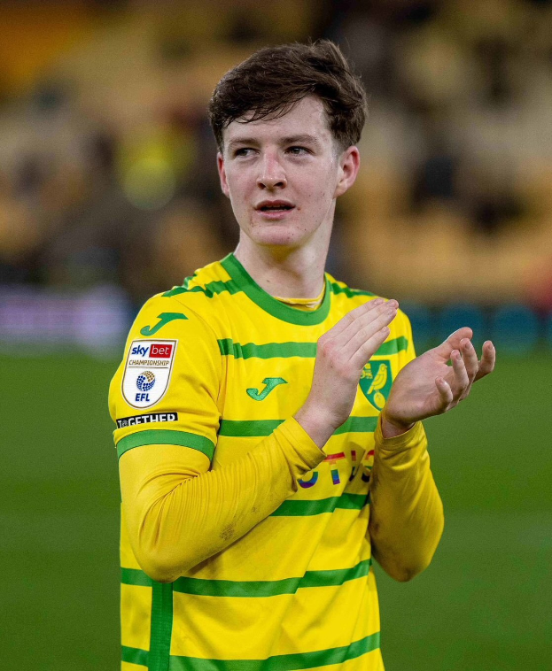 Ein junger Mann in einem gelb-grünen T-Shirt klatscht auf einem Fußballfeld, feiernd ein Tor mit einem unscharfen Hintergrund.