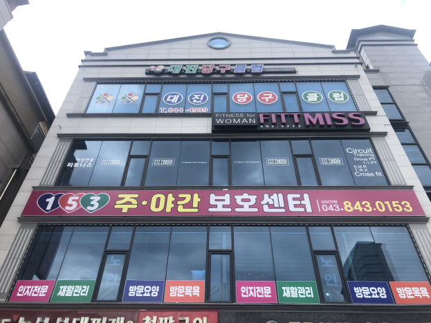 Außenansicht eines Gebäudes in Seoul, Südkorea mit der Aufschrift "Fitness für Frauen", Fenstern und Texttafeln vor einem Himmelhintergrund.