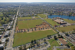 Luftbild einer Stadt mit Gebäuden, Bäumen, Gras, Straßen mit Fahrzeugen, Wasser und Wolken, das einen großen zentralen Bereich zeigt, der als Park vorgeschlagen ist.