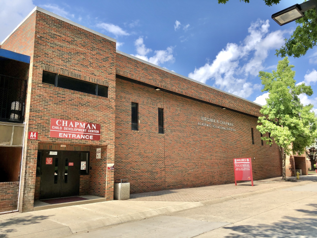 Außenansicht eines Backsteingebäudes mit einem 'Chaplin Kindertagesstätte'-Schild, Fenstern, Türen, einer Namensschilder, einem Müllcontainer, einem Straßenpfosten, Bäumen, parkenden Fahrzeugen und einem bewölkten Himmel.