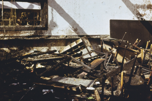 Ein Haufen abgenutzter, verstreuter Holzmöbel vor einem Gebäude mit einer Wand und einem Fenster im Hintergrund.