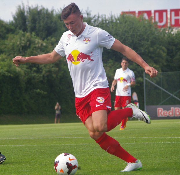 Ein professioneller Fußballspieler, der einen Fußball auf einem grünen Feld kickt, mit "RB Leipzig" im Hintergrund.