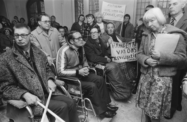 Eine Gruppe von Menschen marschiert mit einem Banner, auf dem "Solidarität und Feminismus" steht, die Straße entlang, mit parkenden Fahrzeugen und Gebäuden im Hintergrund unter einem klaren blauen Himmel.