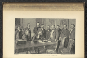 Eine Gruppe von Männern steht um einen Tisch mit Papieren und Gegenständen, ein Mann sitzt in der Mitte, mit Fotorahmen an der Wand im Hintergrund und Text unten, der "Unterzeichnung des Friedensprotokolls in Washington" lautet.