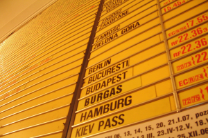 Gelber Wall mit mehreren gelben Schildern, die wahrscheinlich Abfahrts- und Ankunftszeiten für verschiedene Ziele anzeigen.