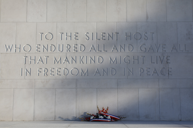 Eine Gedenkwand mit einer Inschrift, die denjenigen ehrt, die für Freiheit und Frieden gelitten und gegeben haben, umgeben von einem Blumenstrauß.