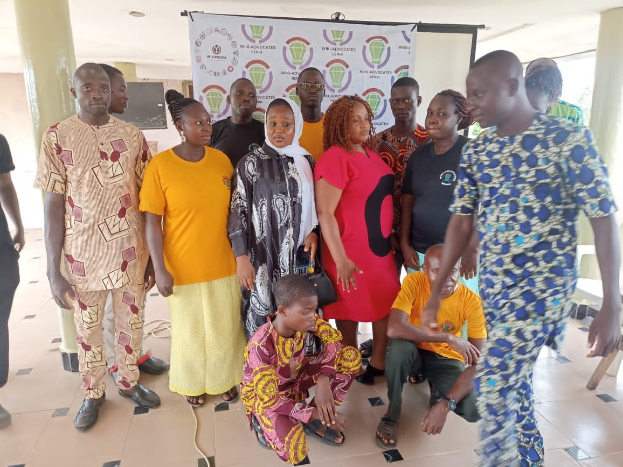 Gruppe von Menschen vor einer Banner stehend, auf dem "Advocates in Ghana: Ein Schritt-für-Schritt-Führer" steht, mit Stühlen, Säulen, einem Fernseher und einer Decke mit Deckenleuchten im Hintergrund.