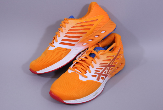 Ein Paar Asics Gel-Nimbus 22 Laufschuhe in Orange, Weiß und Blau, das auf einer grauen Oberfläche platziert ist, mit einem Mesh-Obermaterial, einer gepolsterten Zwischensohle und einer strapazierfähigen Außensohle.