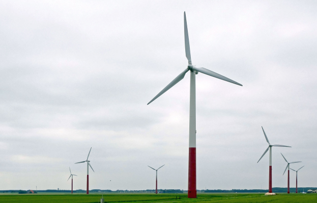 Eine Gruppe hoher, weißer Windkraftanlagen in einem grünen Feld mit Bäumen und Wolken im Hintergrund.