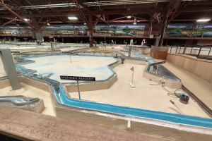 Ein großes Indoor-Wasserpark mit mehreren Wasserrutschen, einem Minigolfplatz, beleuchteter Decke, Wandgemälden und Beschilderung.
