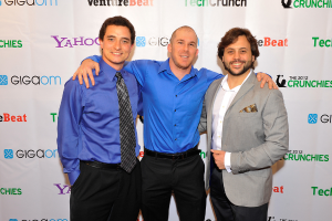 Drei Personen vor einer Sponsoren-Wand mit Kleidung