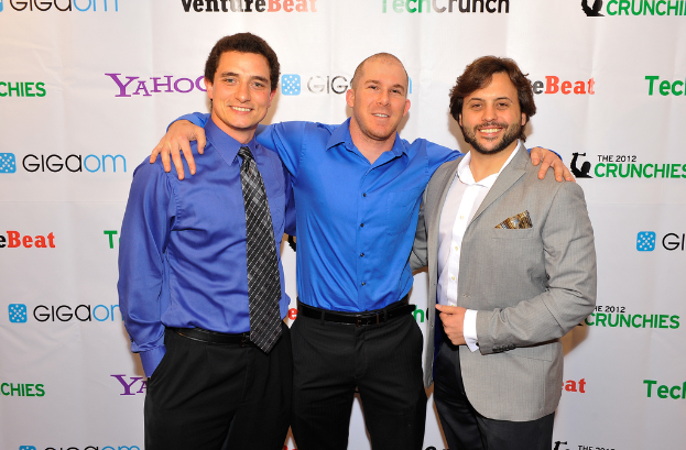 Drei Personen vor einer Sponsoren-Wand mit Kleidung