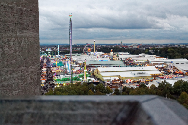 Freizeitpark-Ansicht von einem Turm aus, mit einer Wand, Bäumen, Gebäuden, Fahrgeschäften und Pfählen im Vordergrund und einem bewölkten Himmel im Hintergrund.