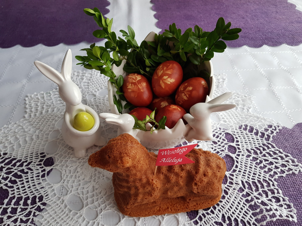 Ein mit einer Decke drapierter Tisch hält eine Schüssel mit bunten Ostereiern und Osterhasenfiguren darauf.
