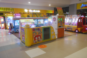 Ein großer Arcade-Raum voller verschiedener Arcade-Automaten, mit einer Decke mit Lichtern, einem Boden und einer Hintergrundwand, der eine Vergnügungspark-Atmosphäre schafft.
