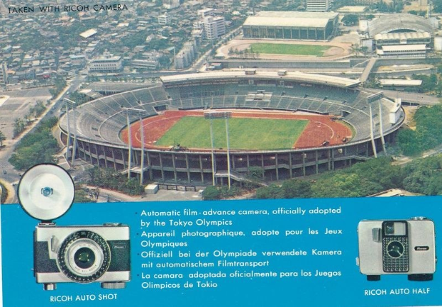 Luftaufnahme eines Stadions mit einer Kamera im Vordergrund, umgeben von Gebäuden, Bäumen und Fahrzeugen, mit einem Plakat mit Text und Kamera-Bildern unten.