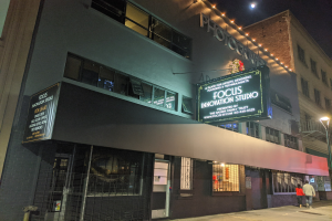 Außenansicht des Focus Innovation Studio in New York City bei Nacht, mit beleuchteten Fenstern und Namensschildern an umliegenden Gebäuden, Menschen auf dem Gehweg und einem sichtbaren Nachthimmel.