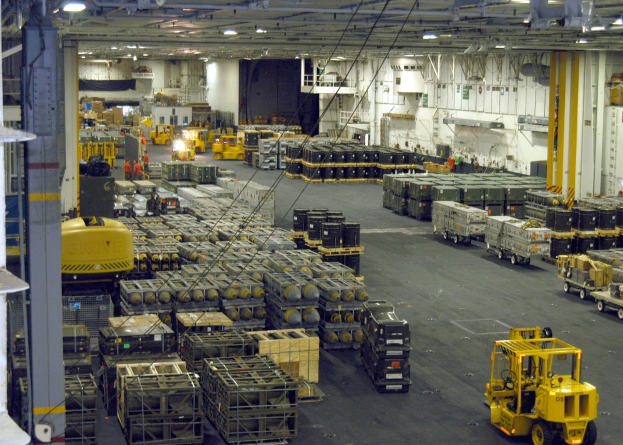 Lagerinneres mit Lkw, Containern, Menschen, Beleuchtung, Metallstangen und einem sichtbaren Rad.