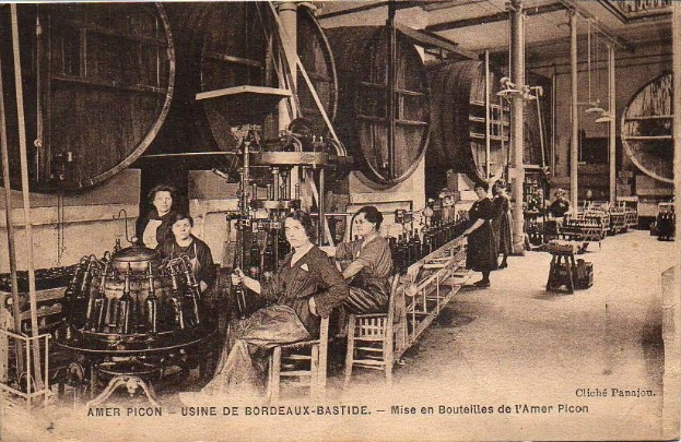 Schwarzes und weißes Foto von Frauen, die in einer Fabrik mit Maschinen und verstreuten Gegenständen arbeiten, einige sitzen und andere stehen, mit dem Text "Amer Picon - Use de Bordeaux-Bastide" unten.
