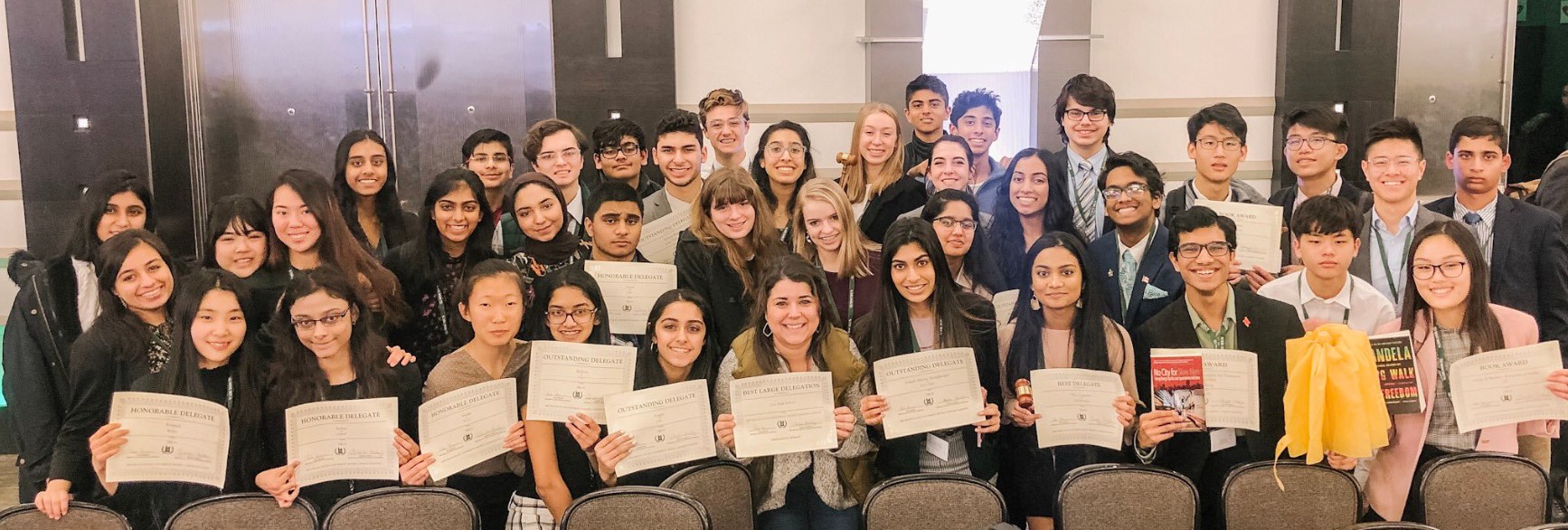 Gruppe von Menschen mit Urkunden in einem Raum mit Stühlen und einer Wand, wahrscheinlich feiern sie eine Abschlusszeremonie für das akademische Jahr 2019-2020.