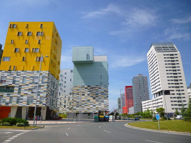 Eine Stadtstraße mit hohen Gebäuden, die als Teil der Universität Rotterdam gekennzeichnet sind, Straßenlaternen, Straßenschilder, Kraftfahrzeuge, Informationsanzeigen, Büsche, Bäume und eine bewölkte Himmel.