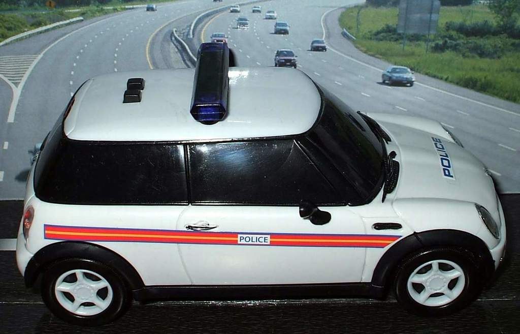 Weißer Polizeiauto mit "Polizei" Aufschrift auf einer Straße außerhalb der Stadt, umgeben von fließendem Verkehr und grasigen Bereichen mit Bäumen auf beiden Seiten.
