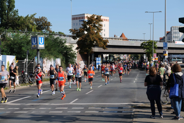 Gruppe von Menschen, die bei einem Marathon auf einer von Bäumen gesäumten Straße laufen.
