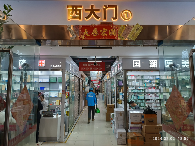 Innenansicht einer chinesischen Apotheke mit Glaswänden, einer Pflanze auf der linken Seite, Regalen mit Gegenständen und einem Namensschild oben.