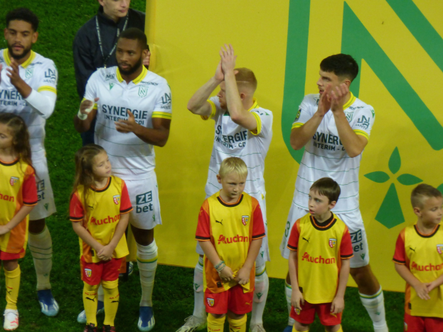 Eine Gruppe von Fußballspielern in Uniformen, die auf einem Feld klatschen, mit einem "Ligue 1"-Schild im Hintergrund, das einen Sieg feiert.