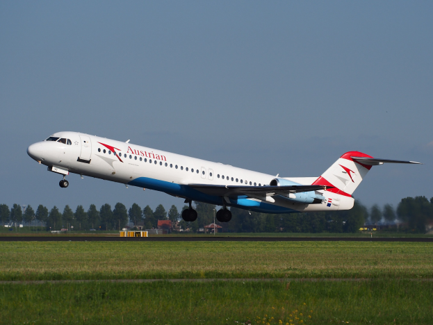 Austrian Airlines Embraer ERJ-190 Flugzeug beim Abheben vom Frankfurt Airport, mit grünem Gras darunter und Bäumen und Gebäuden im Hintergrund.