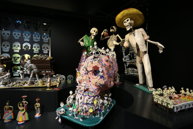 Tag der Toten Ausstellung im Fine Arts Museum in San Francisco mit Spielzeug, Skeletten und Objekten auf Tischen in einer dunklen, mysteriösen Atmosphäre.