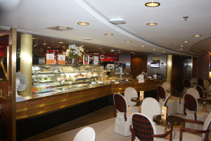 Ein Restaurant-Innenraum mit Tischen und Stühlen, einer Theke mit Blumenvasen, Tafeln mit Text, einem Ventilator und anderen Gegenständen unter einer Decke, die mit warmem Licht beleuchtet ist.