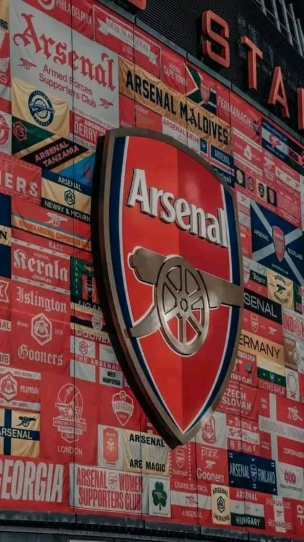 Arsenal FC-Logo an einer Gebäudefassade mit Bannern und Fahnen, begleitet von Texttafeln unten.