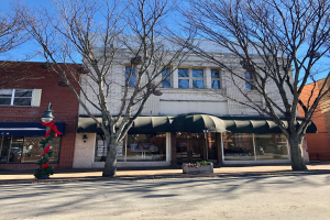 Ein Eckgebäude mit einer grünen Markise, Glasfenstern und einem Namenbrett, auf dem "Citizens Bank and Trust Co." steht, umgeben von Bäumen und einem Lichtmast, mit einem bewölkten Himmel im Hintergrund.