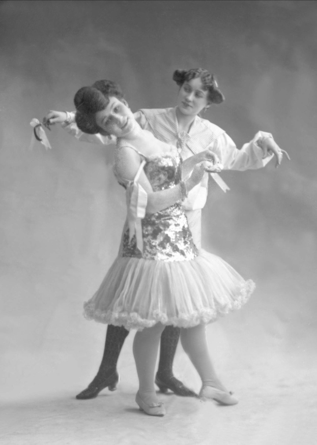 Zwei Frauen auf einem Schwarz-Weiß-Foto, die im Einklang tanzen, eine hält ein Band, tragen Kleider.