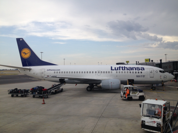 Lufthansa Airbus A320-200 am Frankfurter Flughafen mit Bodenfahrzeugen, Absperrgittern und Beschilderung bei bewölktem Himmel.