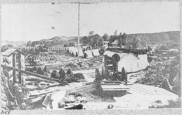 Schwarz-weißes Foto einer Baustelle mit einer Maschine im Vordergrund, umgeben von Hütten, Bäumen, Hügeln und Himmel im Hintergrund, und Text unten, der besagt: "Der Bau einer neuen Brücke in der Stadt San Francisco, Kalifornien."