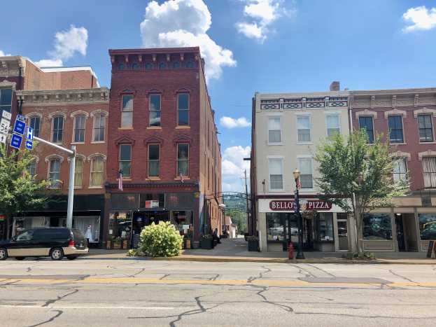 Eine Stadtstraße mit parkenden Autos, Gebäuden, Bäumen, Laternen, Schildern und einem Feuerhydranten unter einem bewölkten Himmel, die ein kommerzielles Objekt zum Verkauf zeigt.