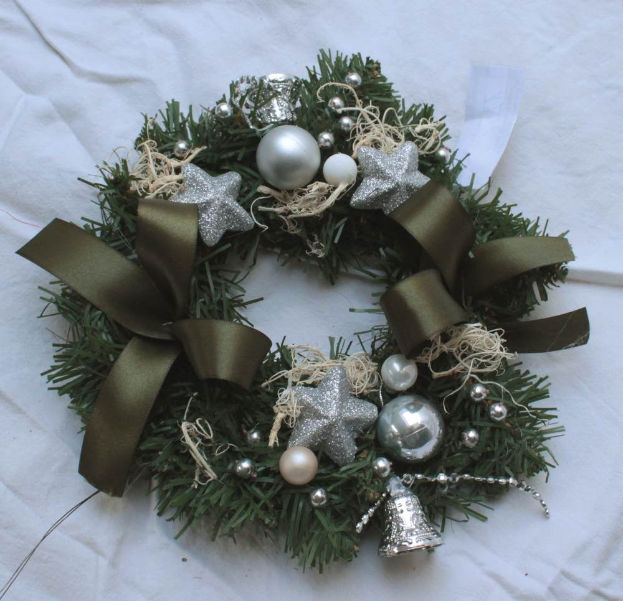 Ein festliches Adventsgesteck mit silbernen Schmuckelementen und Bändern auf einem weißen Tuch, mit bunten Kugeln, Sternen und anderen Dekorationen.