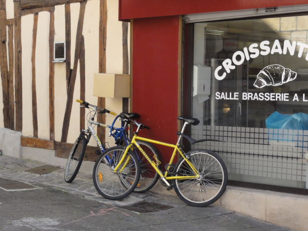 Zwei Fahrräder nebeneinander auf einem Gehweg vor einem Laden mit einer Glaswand mit Text und einem Objekt links von den Fahrrädern.