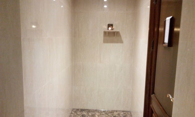 Ein Badezimmer mit einer Duschkabine neben einem WC, mit gefliesten Wänden, Deckenleuchten und einer Tür auf der rechten Seite.