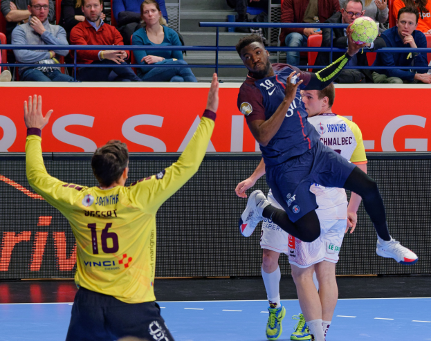 Mannergruppe spielt Hallenhandball auf einem Court mit einem Ball in der Luft, in einer Stadionatmosphäre mit Zuschauern und einer Tafel, die "Futsal-Weltmeisterschaft 2019 - Paris Saint-Germain vs Bordeaux" anzeigt.