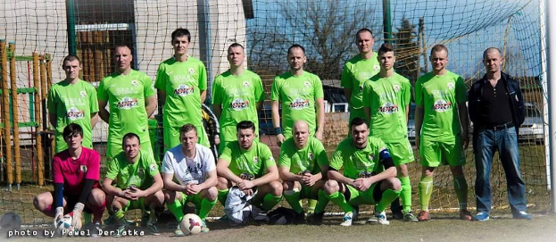 Mannergruppe in grünen T-Shirts auf einem Fußballfeld in der Nähe eines Torpfostens mit einem Ball davor.