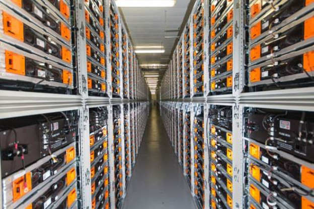 Eine lange Reihe von Servern in einem Rechenzentrum mit elektronischen Geräten in den Gestellen und Leuchten oben.