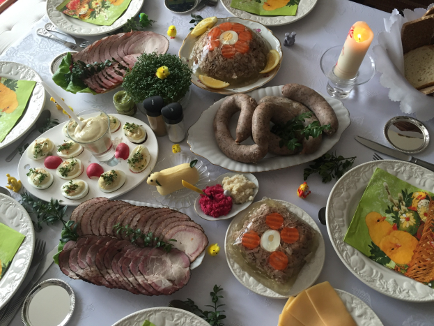 Ein langer Tisch mit einer Vielfalt an deutschen Ostergerichten, umgeben von Stühlen, mit Tellern, Schüsseln, Besteck, Gläsern und Kerzen.