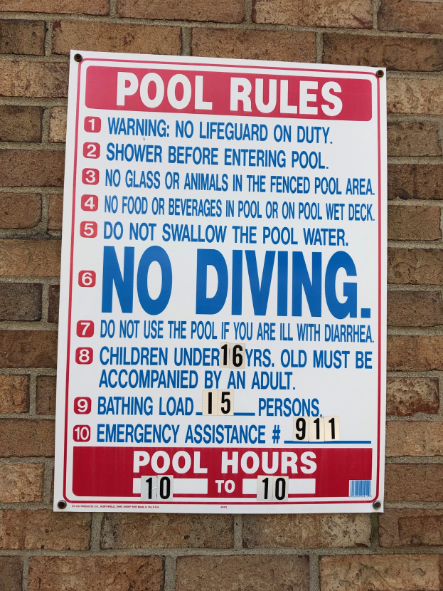 Weißes Schild mit schwarzer Schrift, auf dem "Pool Rules: No Diving" steht, an der Seite eines Backsteingebäudes angebracht
