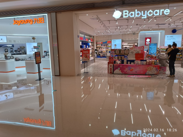 Innenansicht eines Babypflegegeschäfts im Mall of Asia mit Regalen voller Produkte, einem Anzeigebildschirm, Deckenleuchten und einer Gruppe von Menschen, die sich Spielzeug und Gegenstände anschauen.