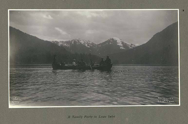 Schwarz-weißes Foto einer Familie in einem Kanu auf einem See mit Bergen und Bäumen im Hintergrund, Himmel oben sichtbar und Text unten.